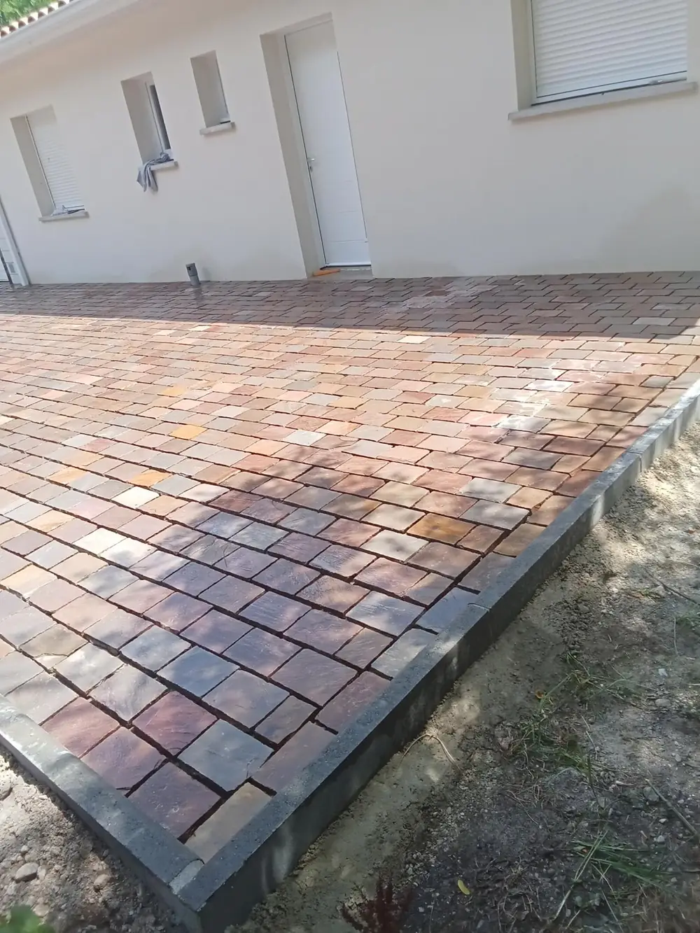 Terrasse pavée avec bordure béton devant une maison